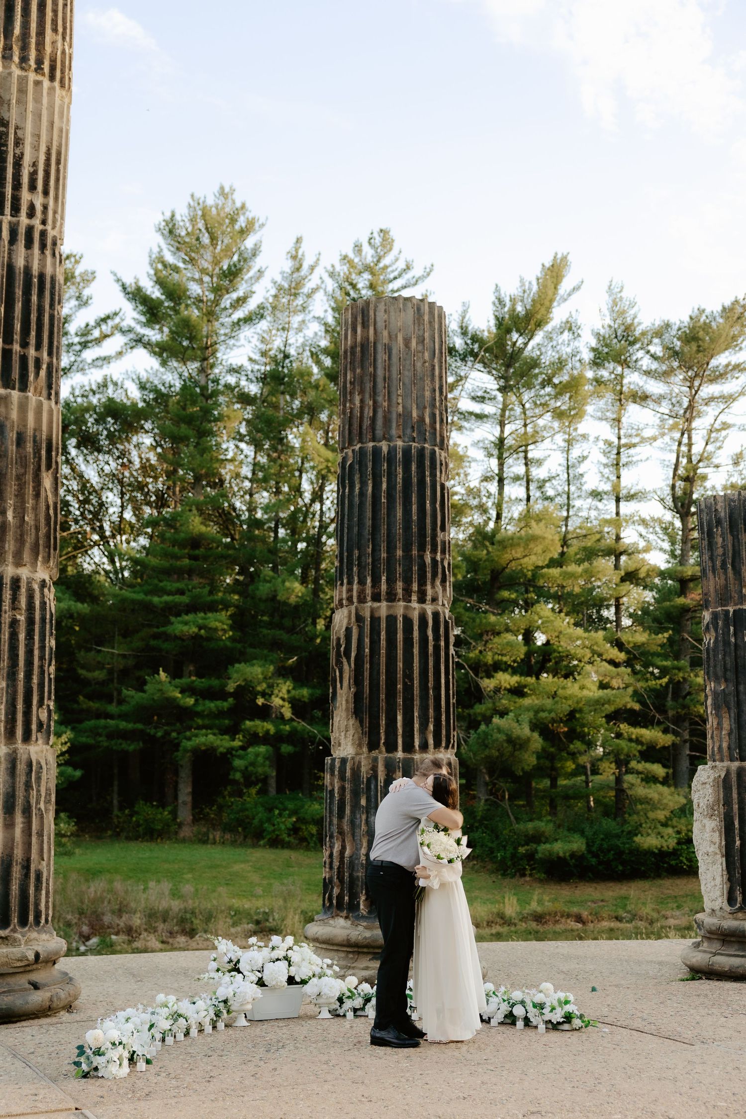 Couple shares romantic moment against stone pillars at sunset during outdoor wedding photoshoot.