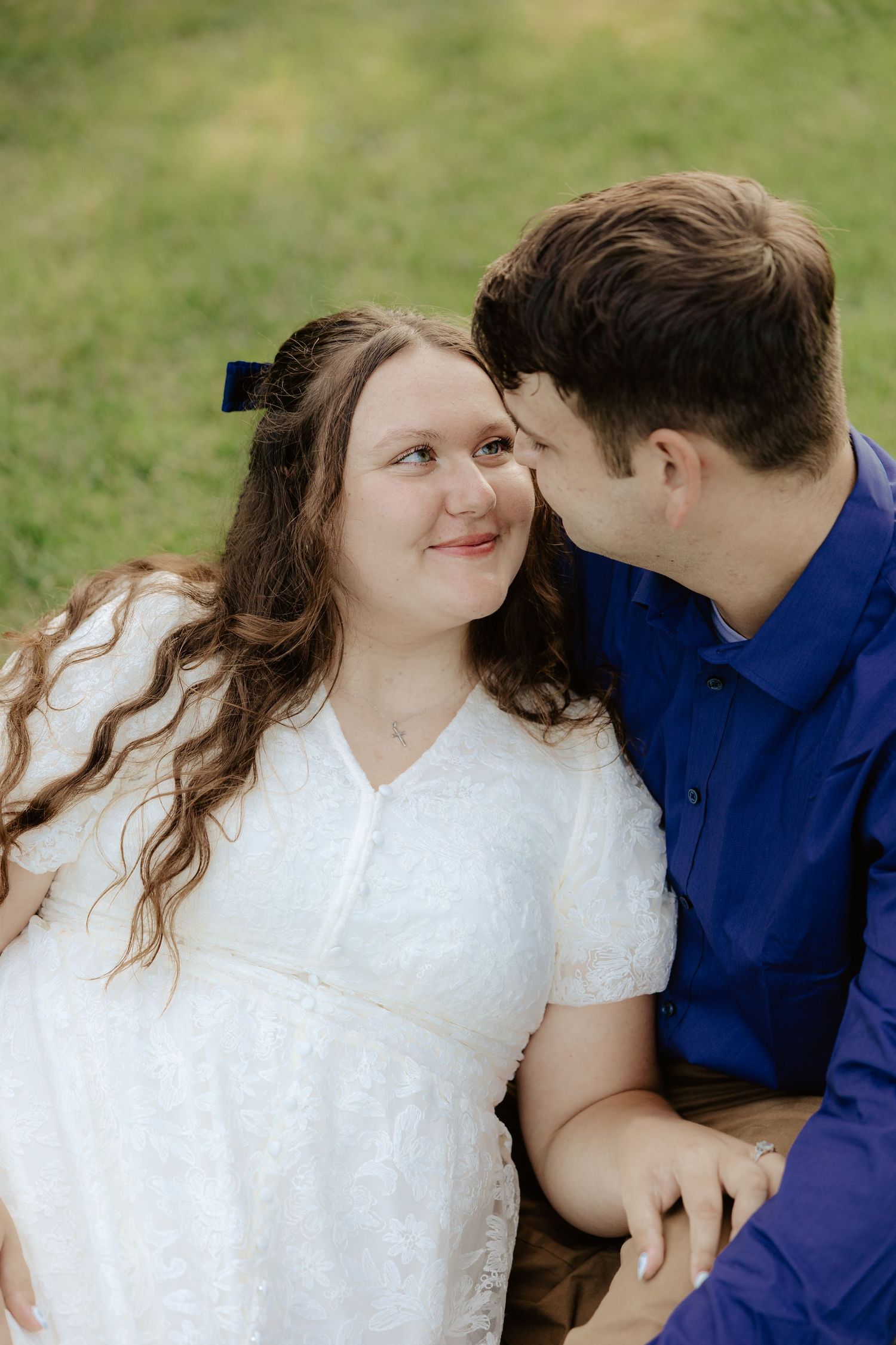 A couple sits together on grass in a natural outdoor setting surrounded by green trees and foliage at Pioneers Park in Lincoln Nebraska.