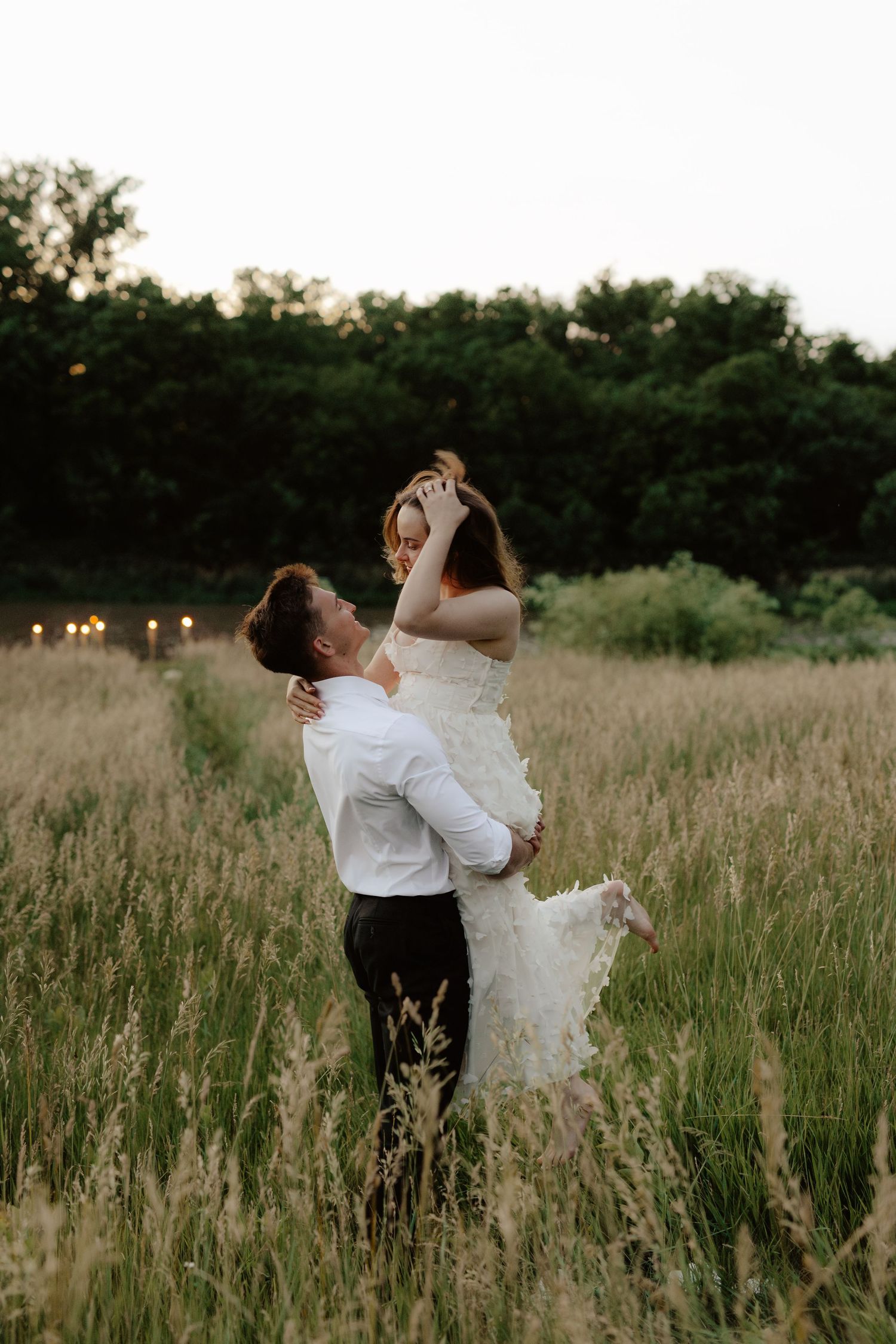 A joyful couple share a romantic proposal moment in a golden sunset field with tall grass and trees in the background.