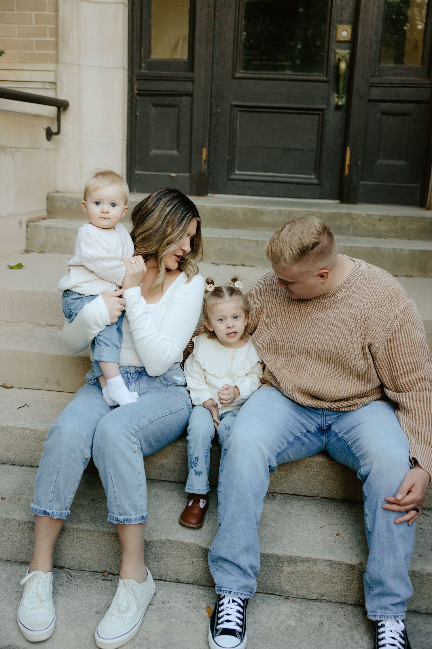 A family sits together on concrete steps outside a building during a family photo session.