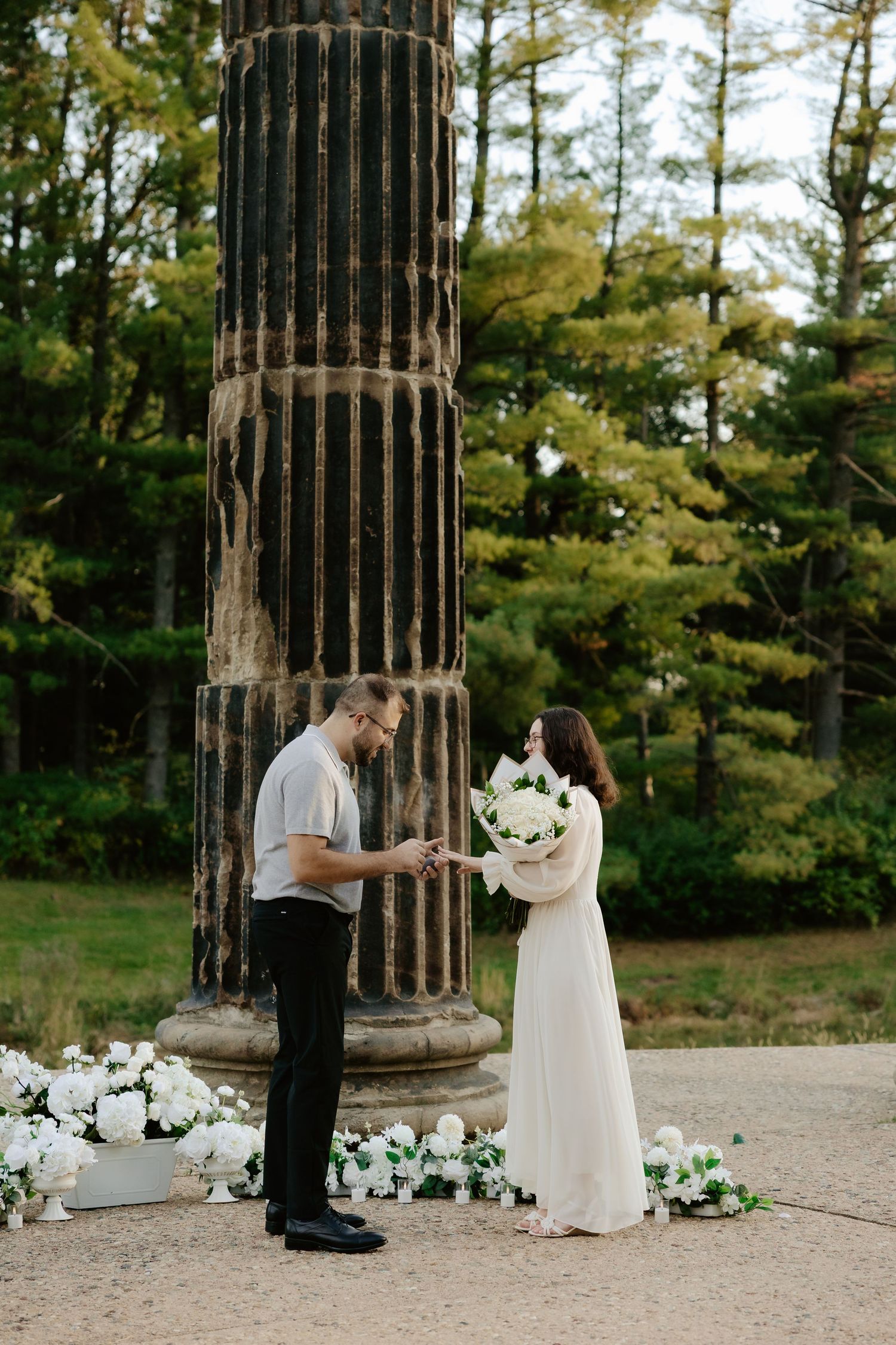 Couple shares romantic moment against stone pillars at sunset during outdoor wedding photoshoot.