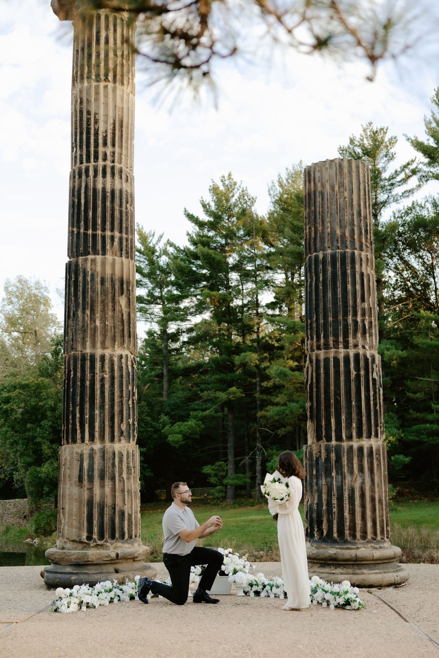Couple shares romantic moment against stone pillars at sunset during outdoor wedding photoshoot.