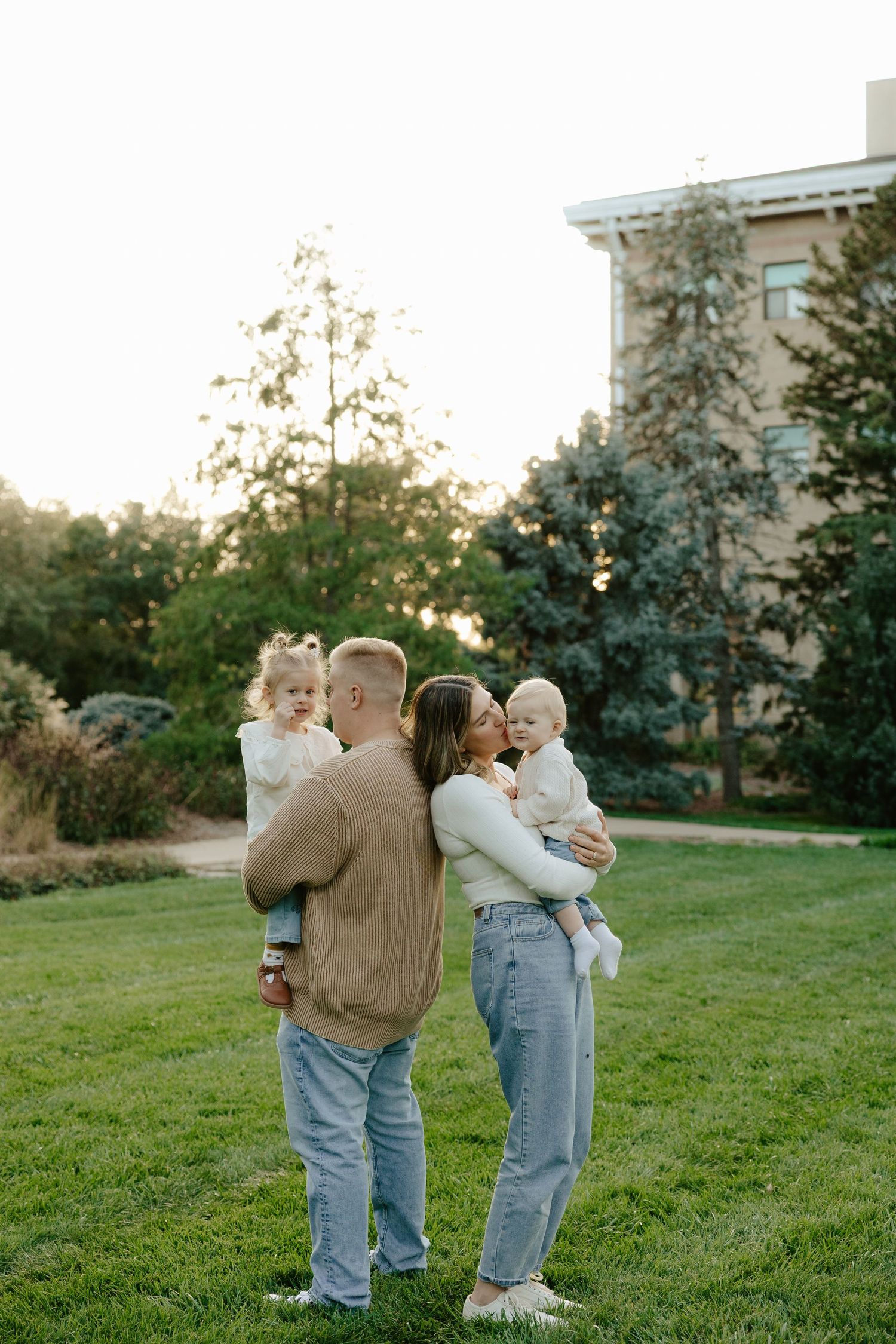 A family shares tender moments together while standing on a grassy lawn during golden hour.