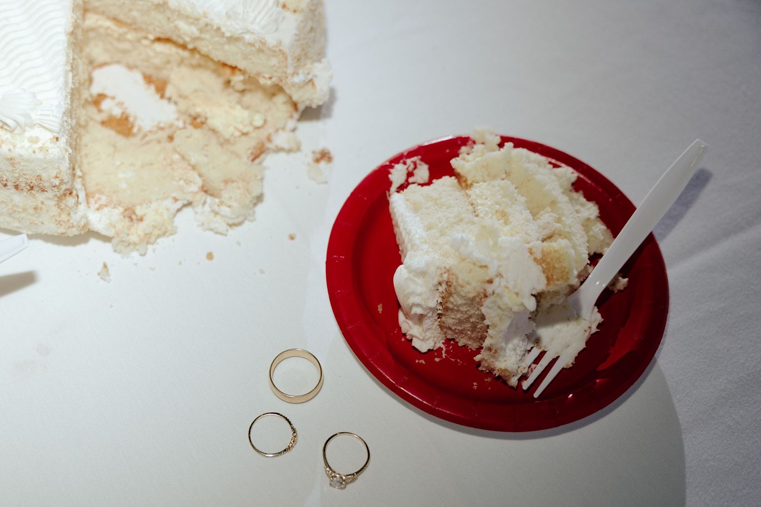 Wedding cake cutting with wedding rings laying on table.