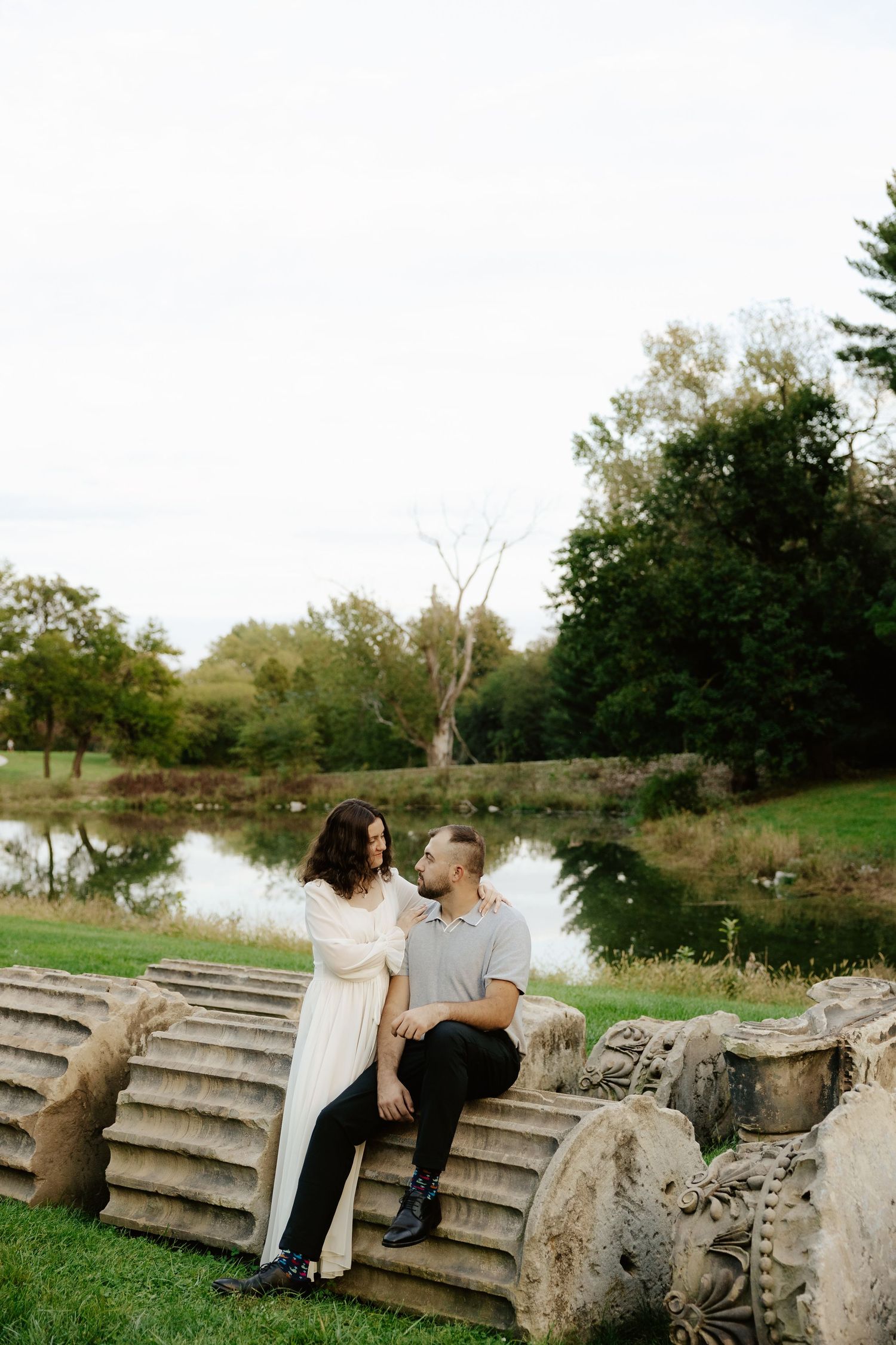 Couple shares romantic moment against stone pillars at sunset during outdoor wedding photoshoot.