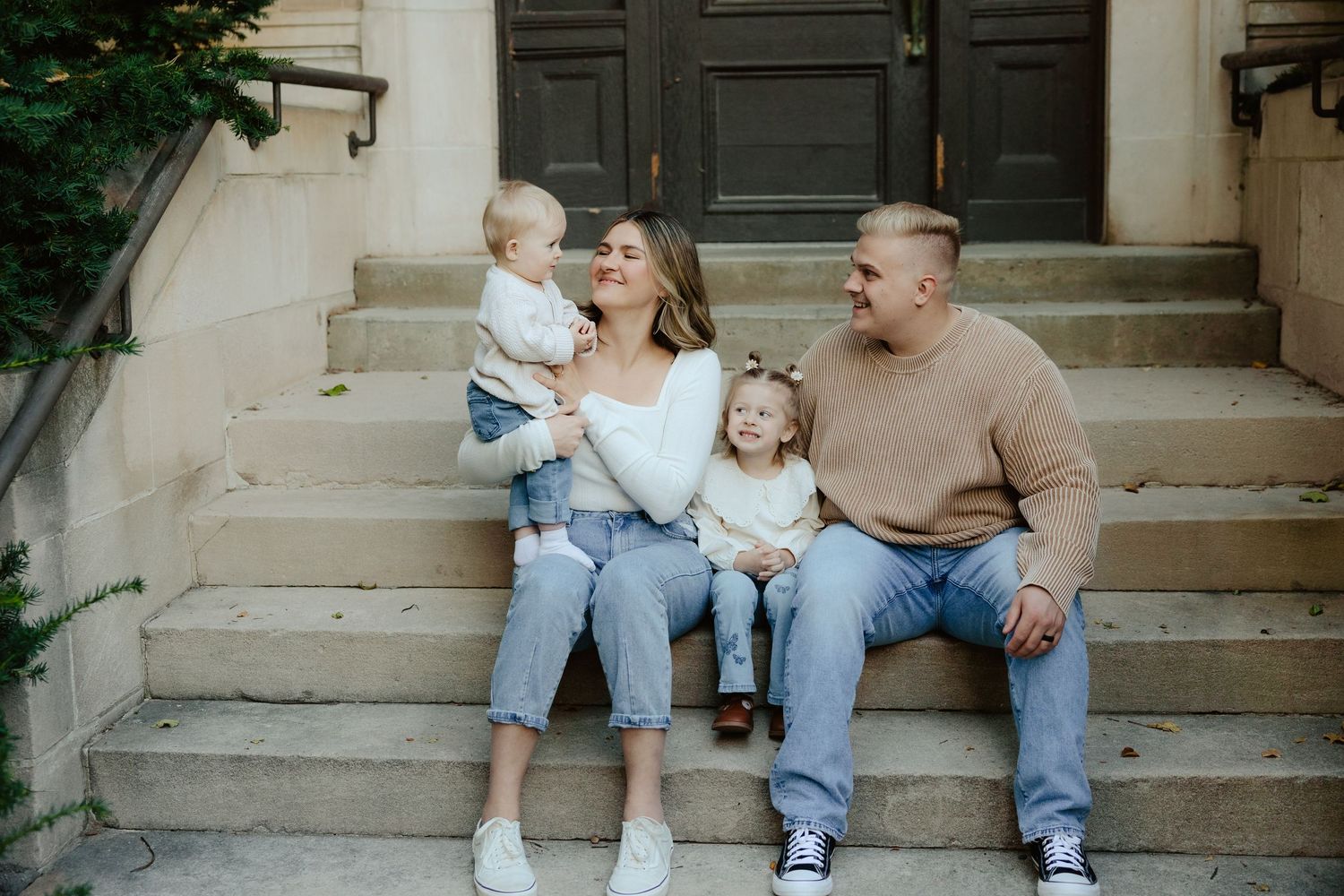 A family sits together on concrete steps outside a building during a family photo session.