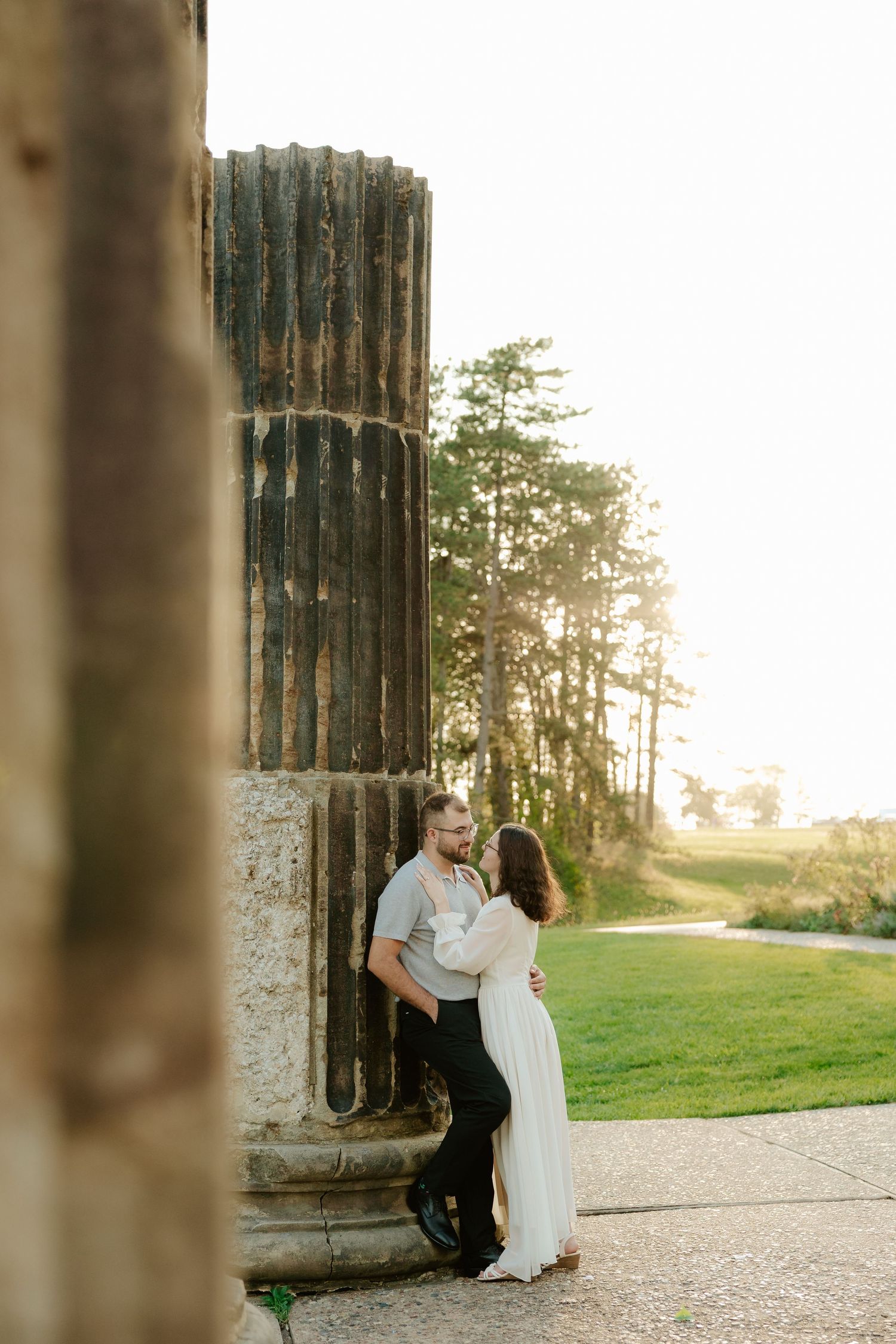 Couple shares romantic moment against stone pillars at sunset during outdoor wedding photoshoot.