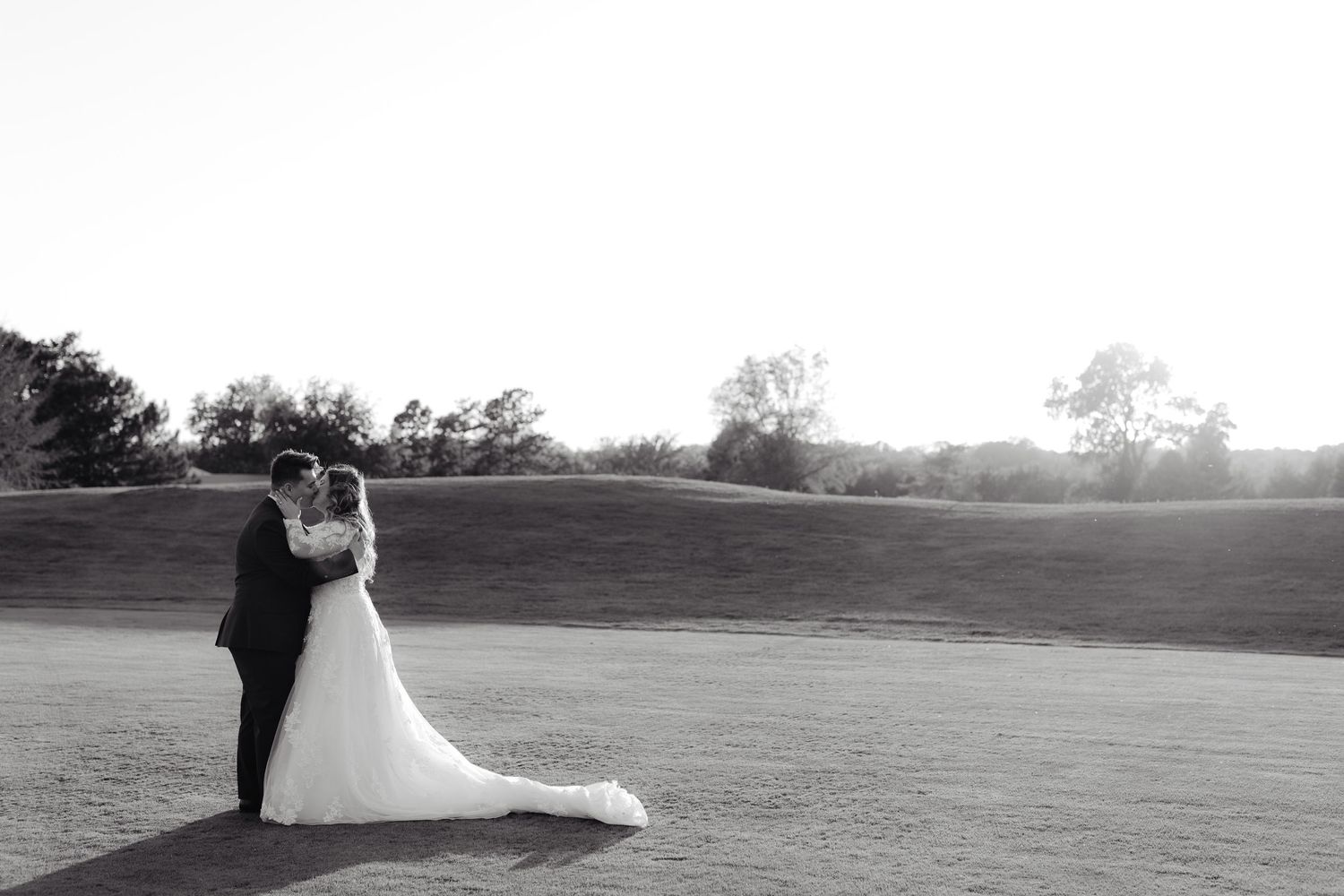A romantic silhouette of newlyweds embracing on a golf course against the sunlight in black and white photography at the Wilderness Ridge