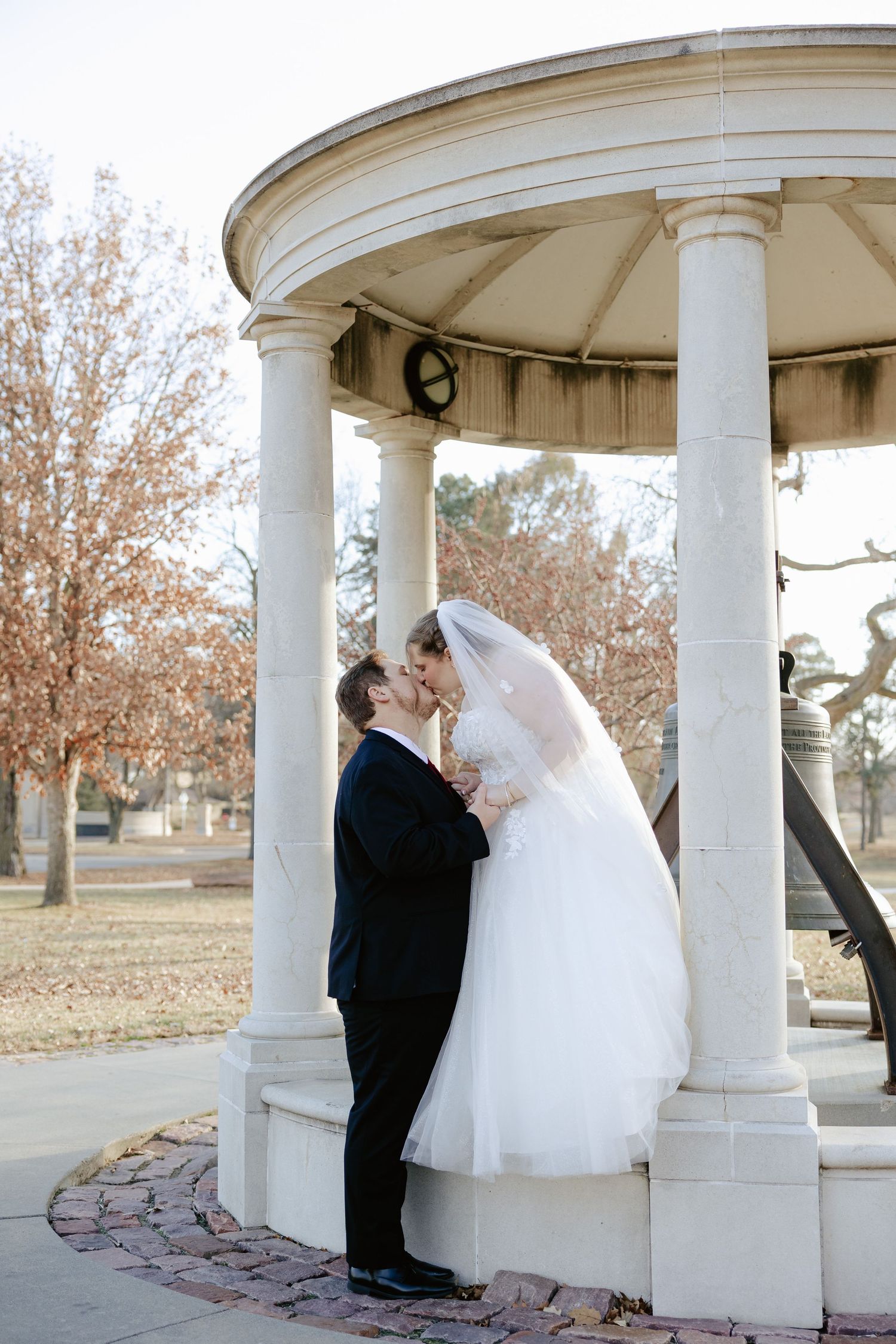 auld pavillion wedding in lincoln nebraska, bride and groom kissing by the bell statue, lincoln nebraska outdoor winter wedding