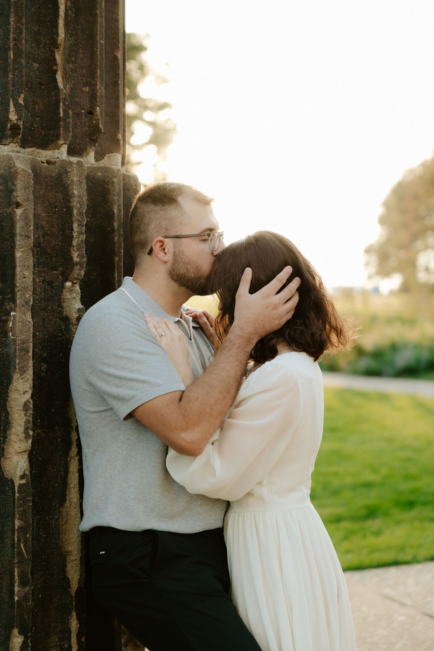 Couple shares romantic moment against stone pillars at sunset during outdoor wedding photoshoot.