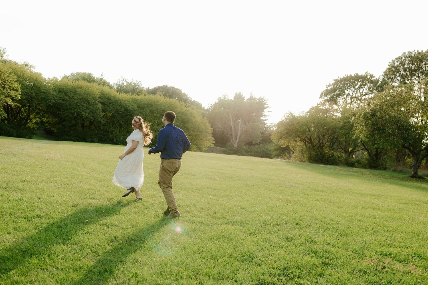 A couple engage in playful interaction across a grassy hillside during a warm sunset  engagement photoshoot.