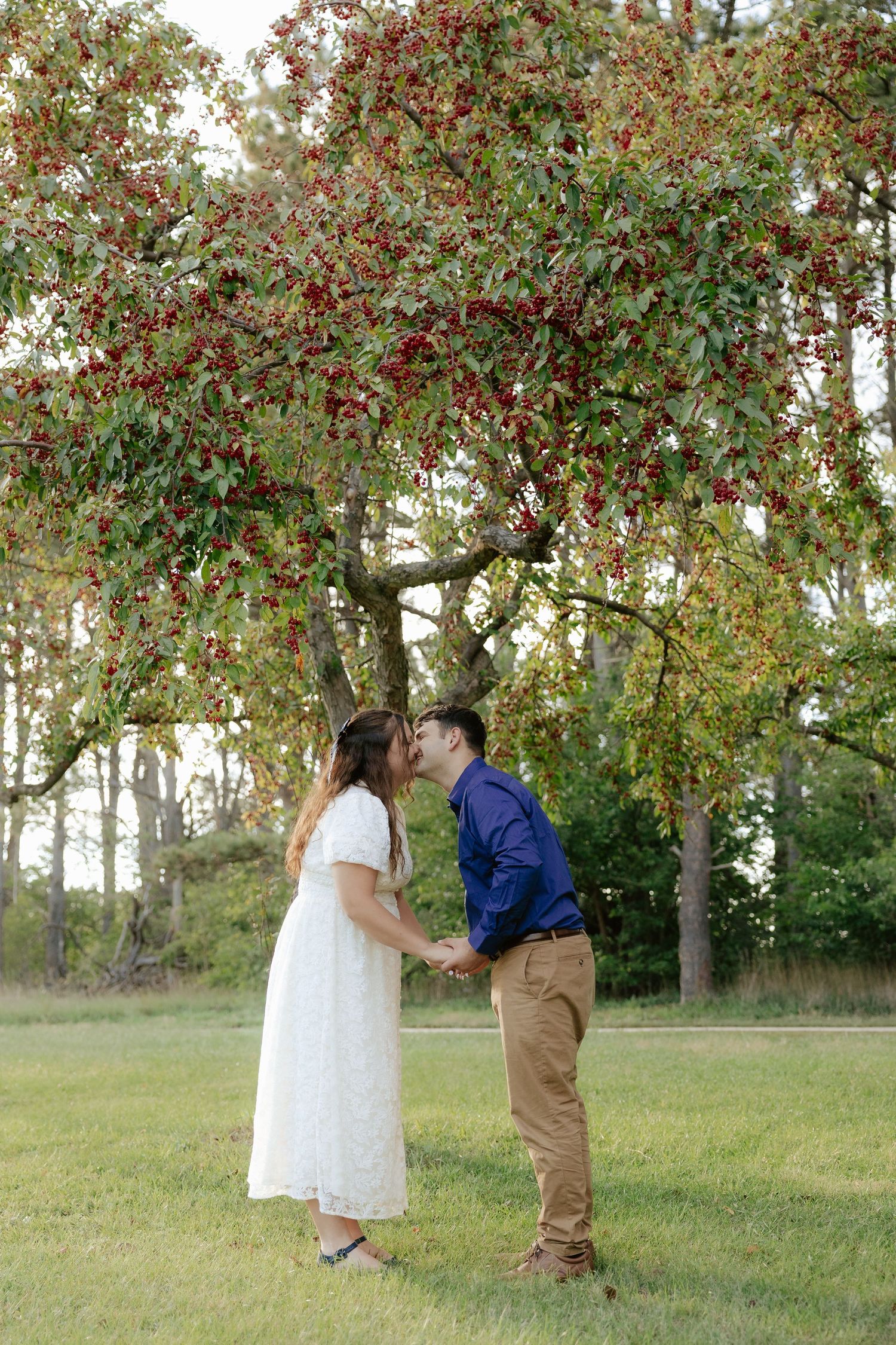 A couple shares a tender moment under a blooming apple tree during their engagement photo shoot.