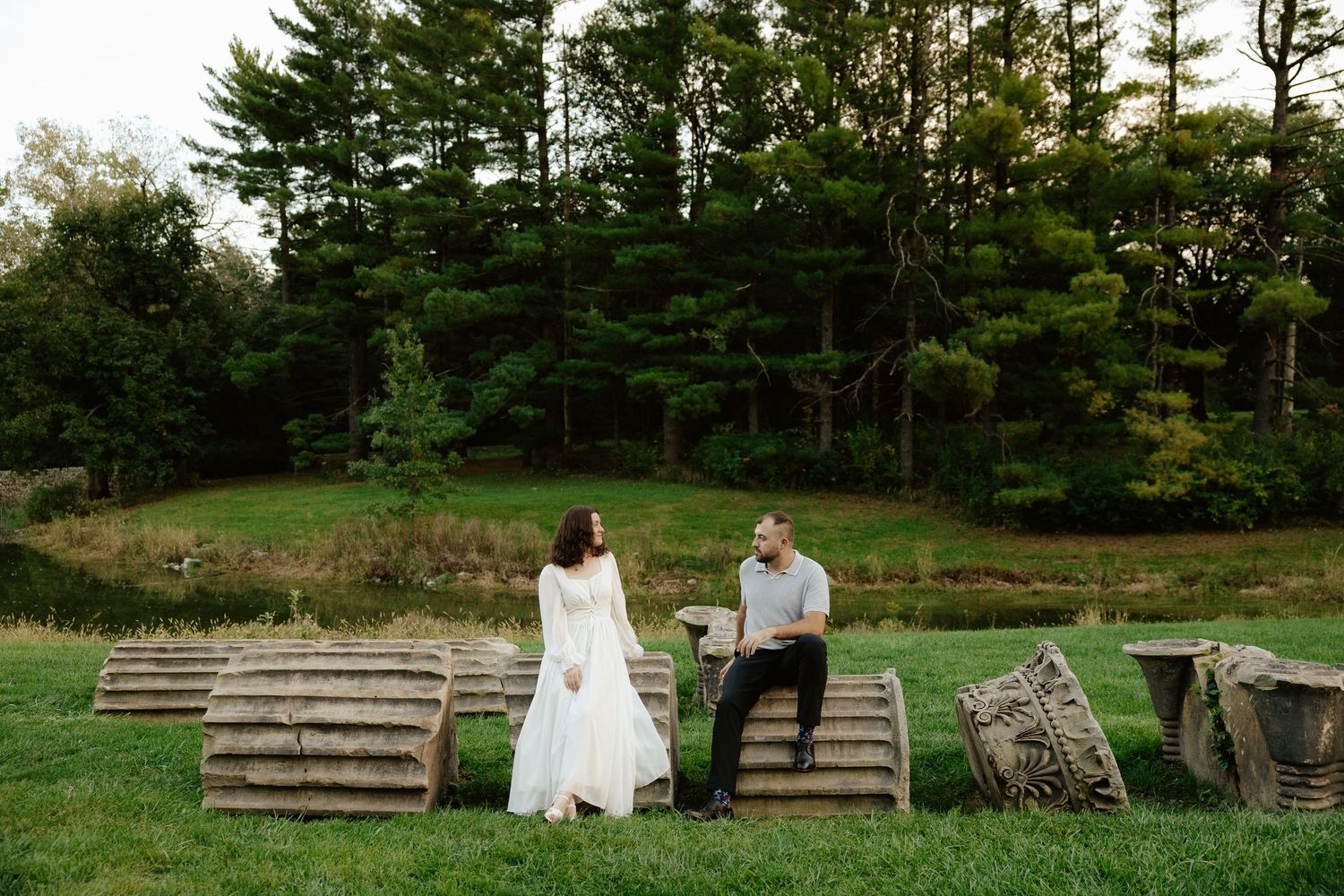 Couple shares romantic moment against stone pillars at sunset during outdoor wedding photoshoot.