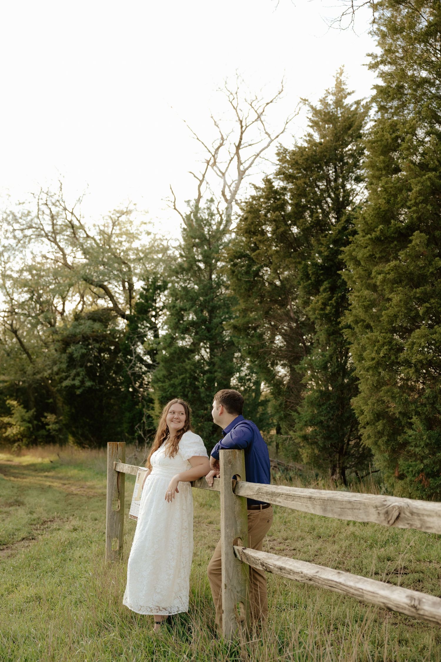 A couple embraces tenderly in an outdoor setting while wearing blue and white outfits in golden sunlight.