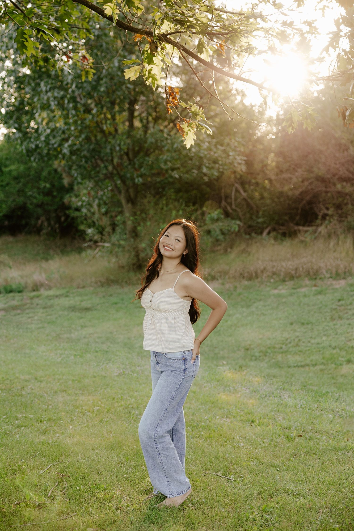 A girl walking through a grassy field in casual clothing at sunset for her senior photo session.