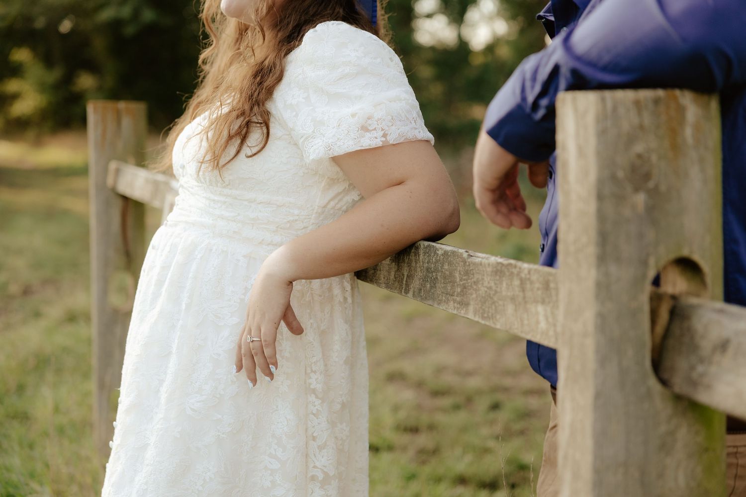 A couple embraces tenderly in an outdoor setting while wearing blue and white outfits in golden sunlight.