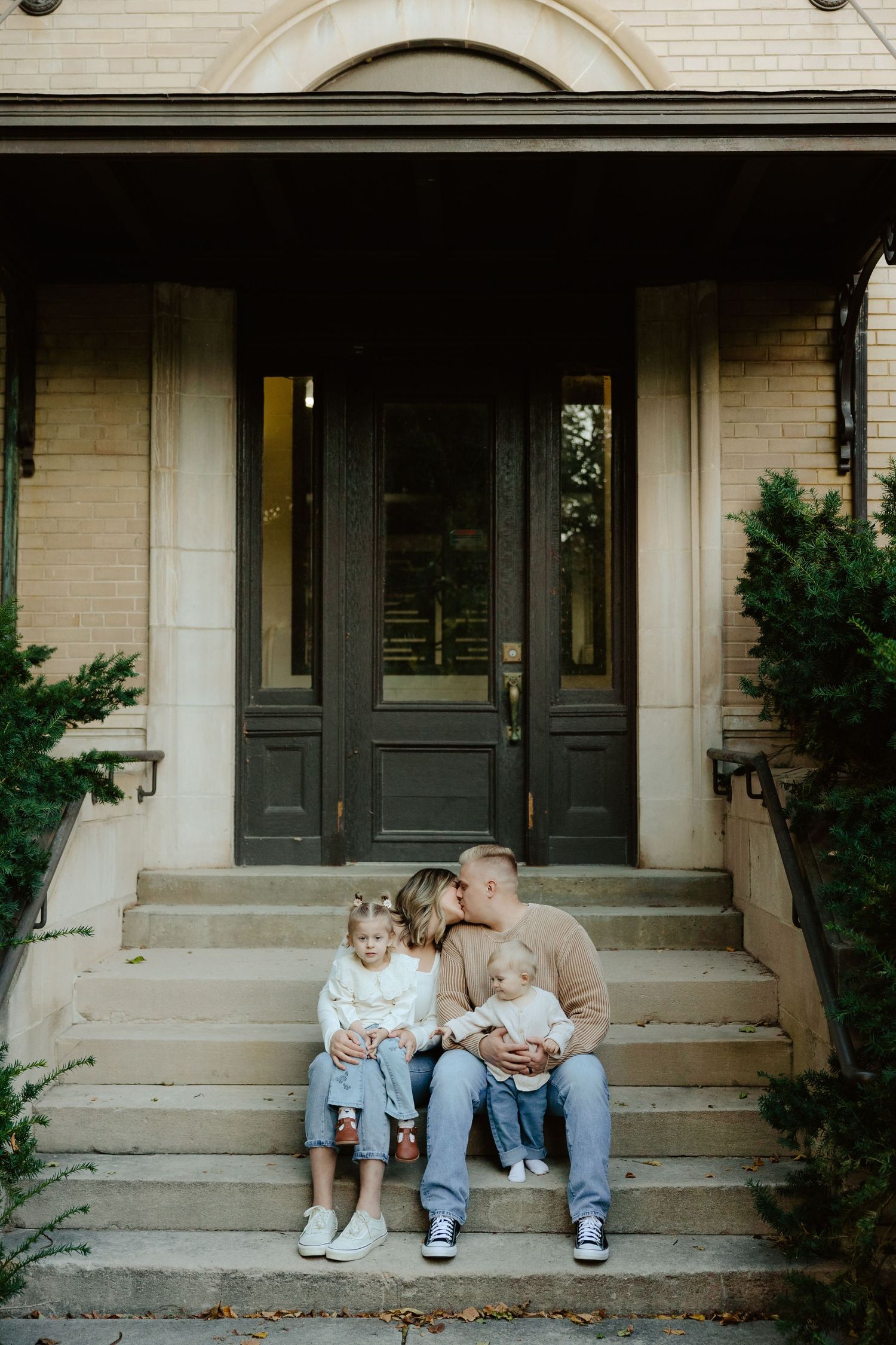 A family sits together on concrete steps outside a building during a family photo session.