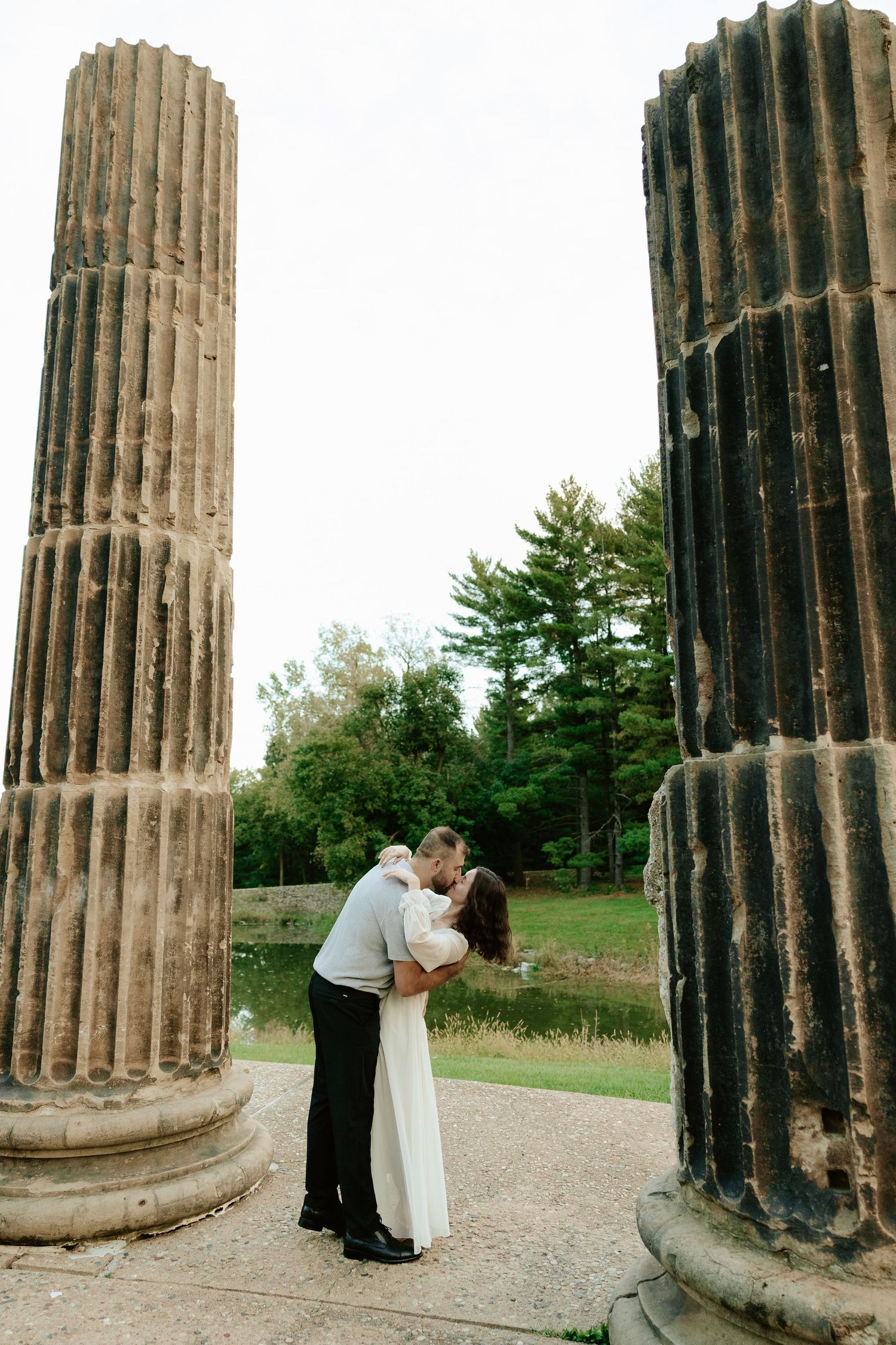Couple shares romantic moment against stone pillars at sunset during outdoor wedding photoshoot.