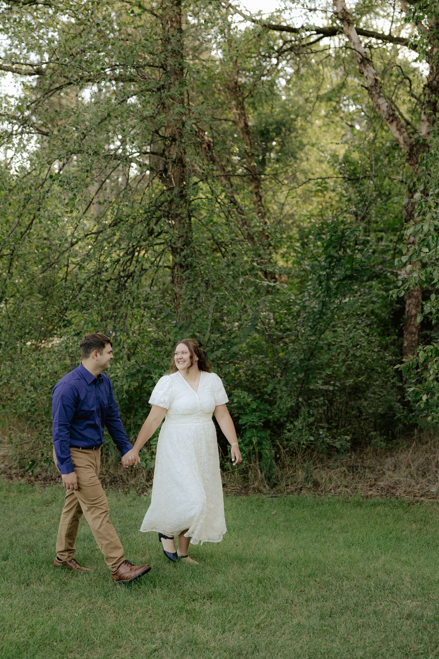 A couple walking hand in hand through lush green foliage on a summer afternoon.