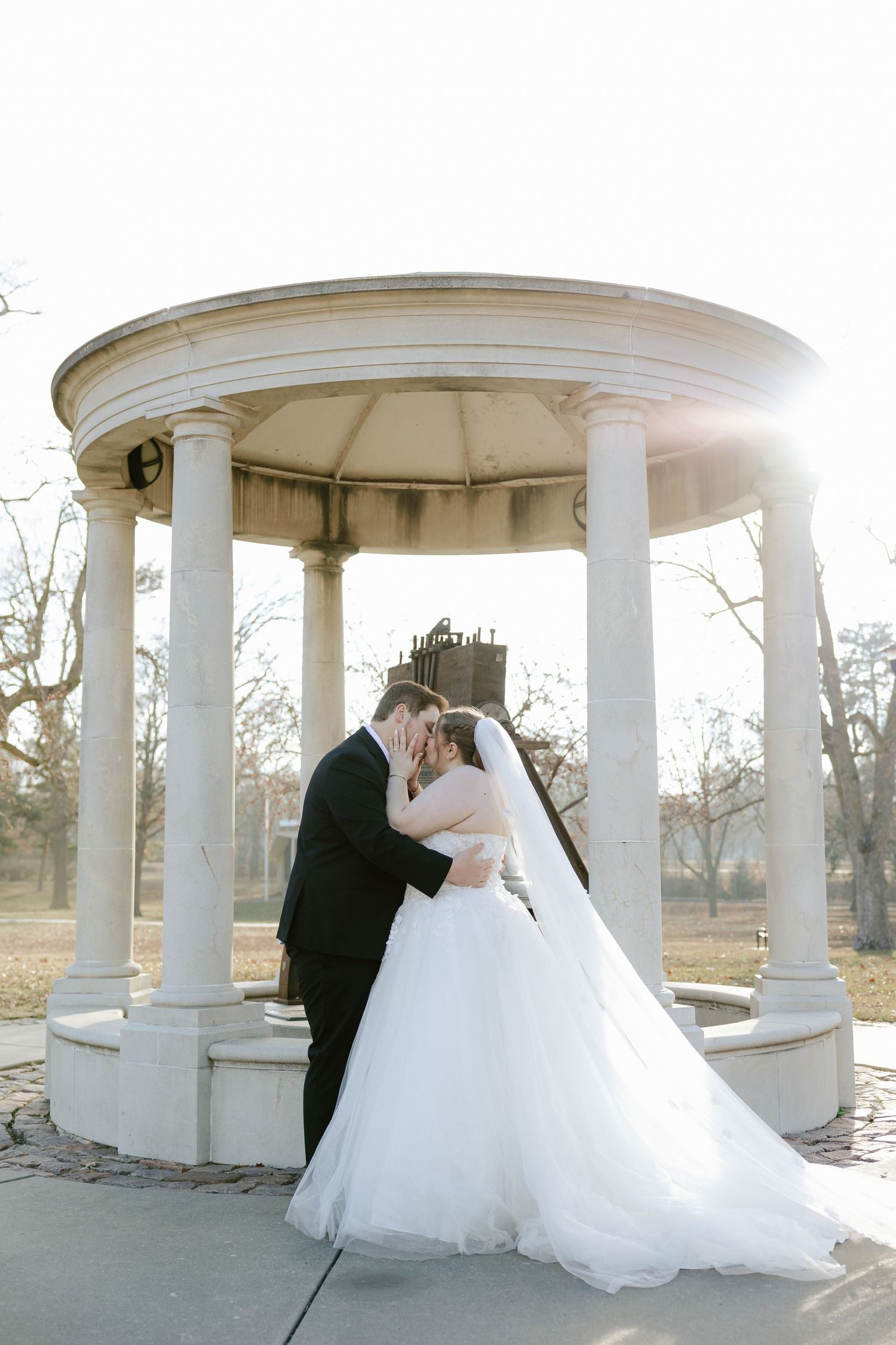 A romantic wedding couple shares an intimate moment under a white columned gazebo at the Auld Pavilion in Antelope Park, Lincoln Nebraska.