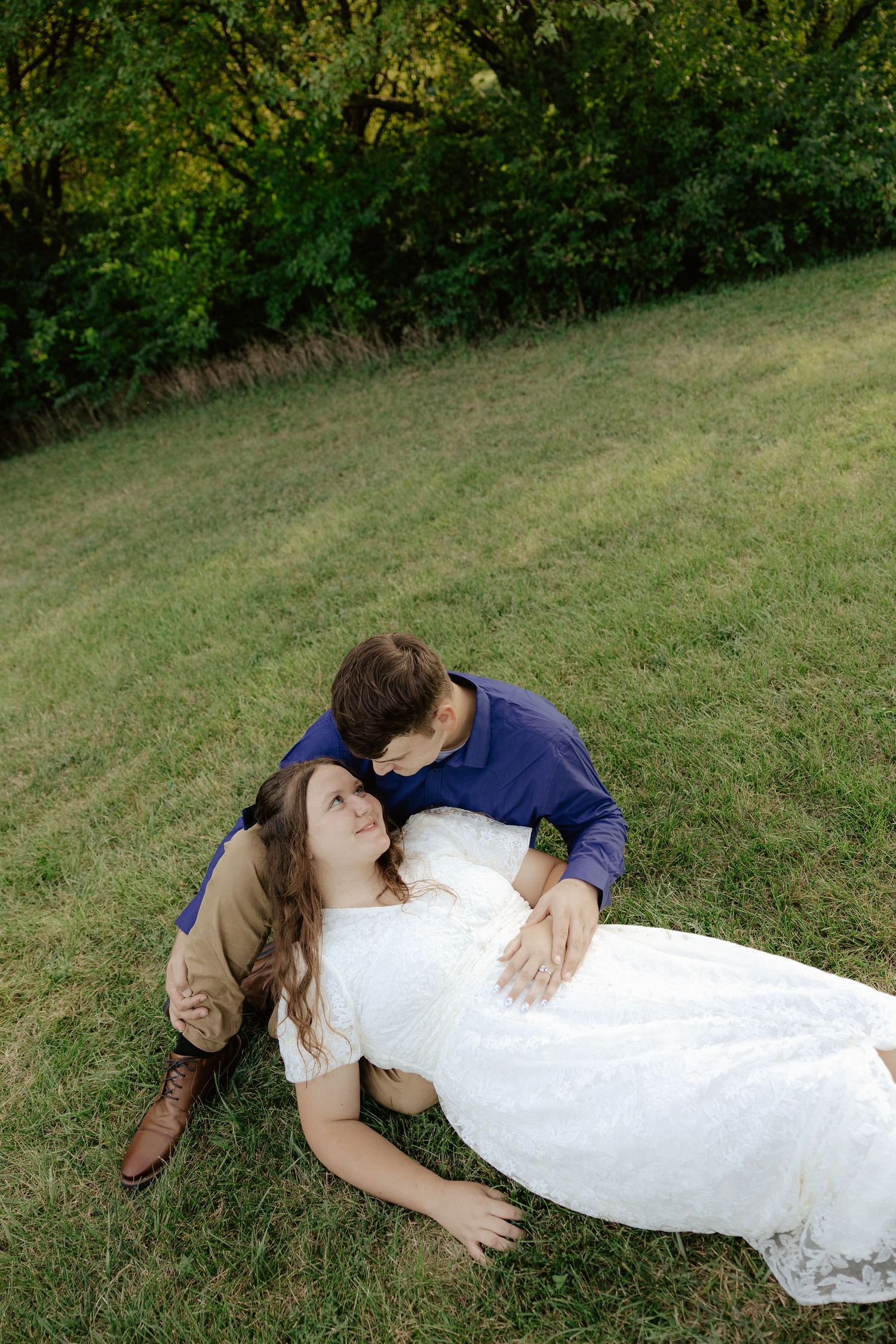 Couple in formal attire lying on green grass in a romantic pose during an outdoor photo session.