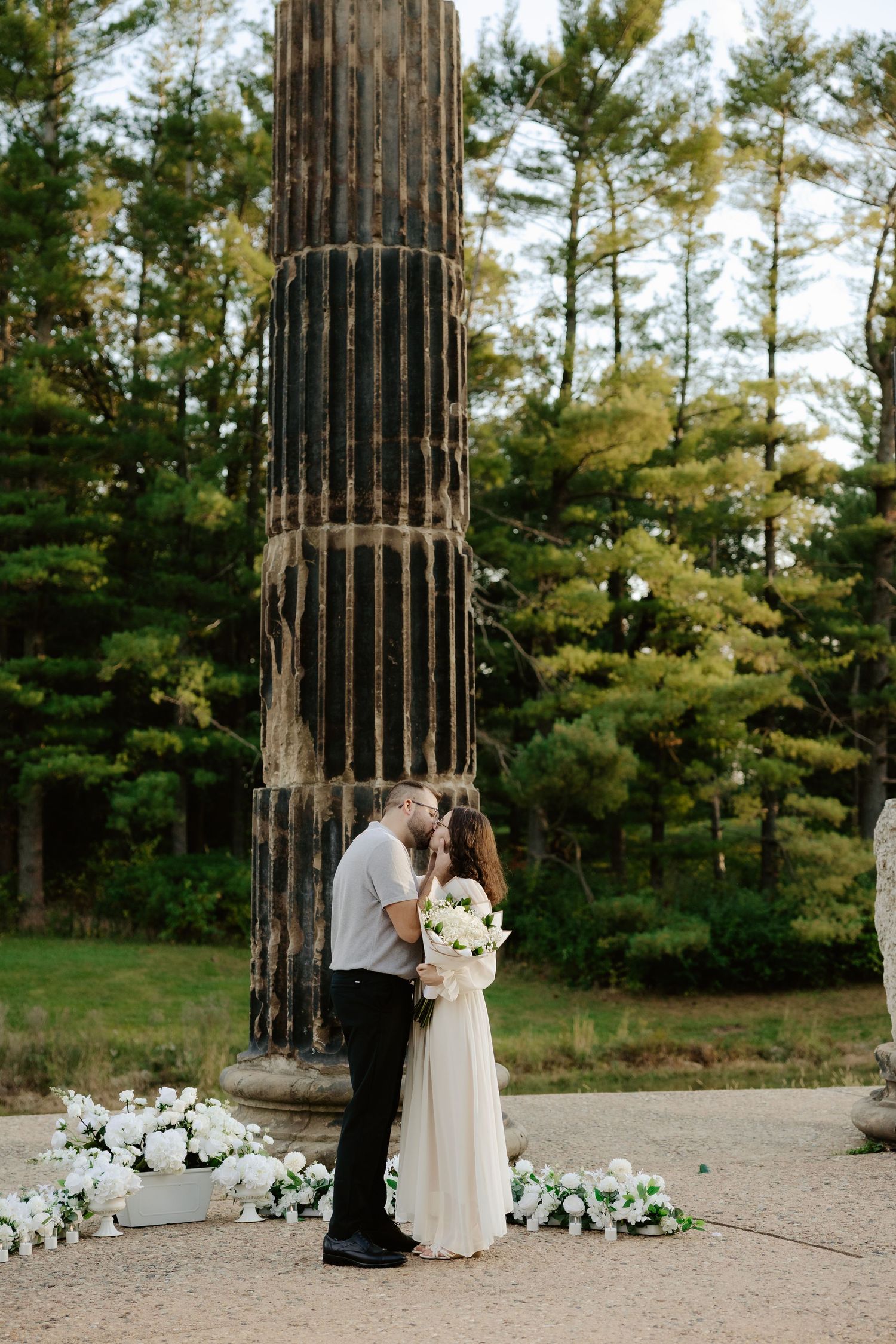 Couple shares romantic moment against stone pillars at sunset during outdoor wedding photoshoot.
