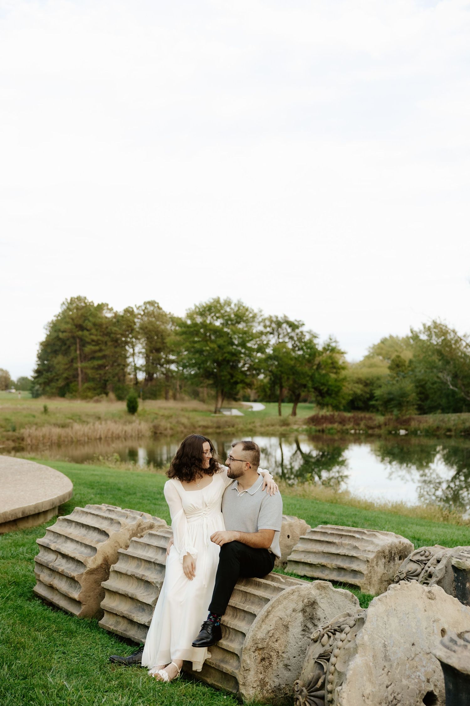 Couple shares romantic moment against stone pillars at sunset during outdoor wedding photoshoot.