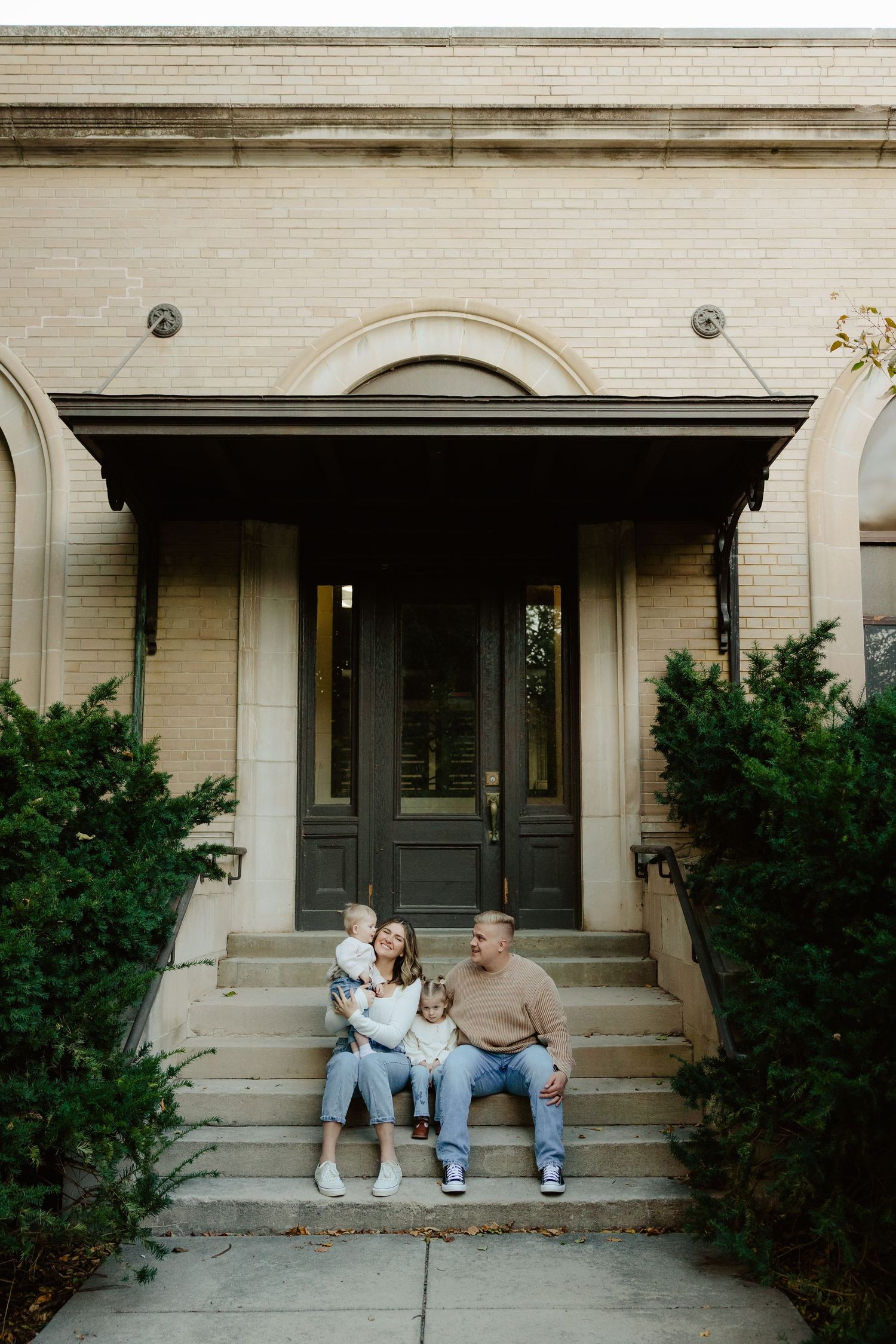 A family sits together on concrete steps outside a building during a family photo session.