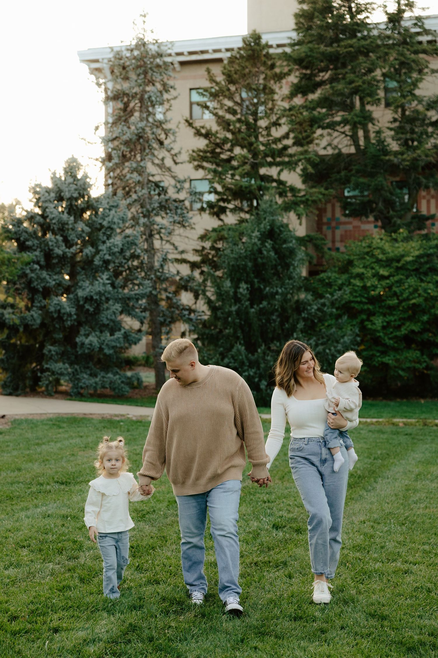 A family walks together holding hands across a green lawn with buildings visible in the background.
