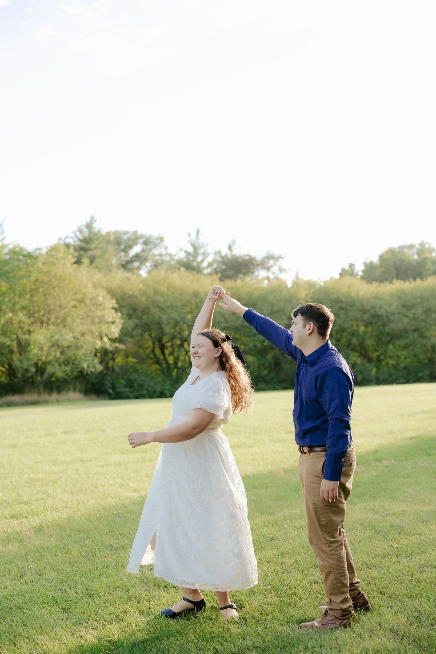 A couple engage in playful interaction across a grassy hillside during a warm sunset  engagement photoshoot.