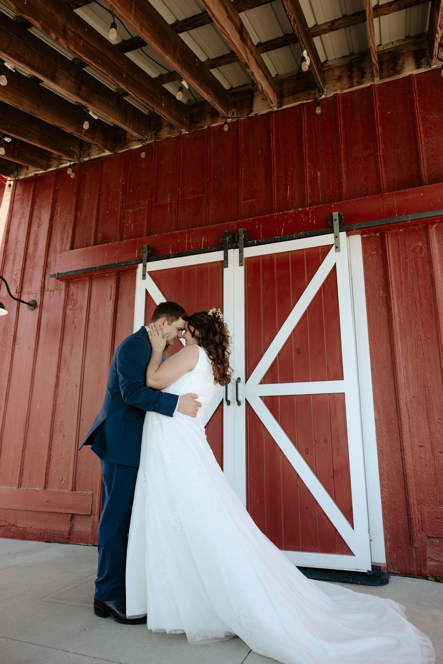 Bride and groom sharing a kiss in front of a rustic red barn door on their wedding day.
