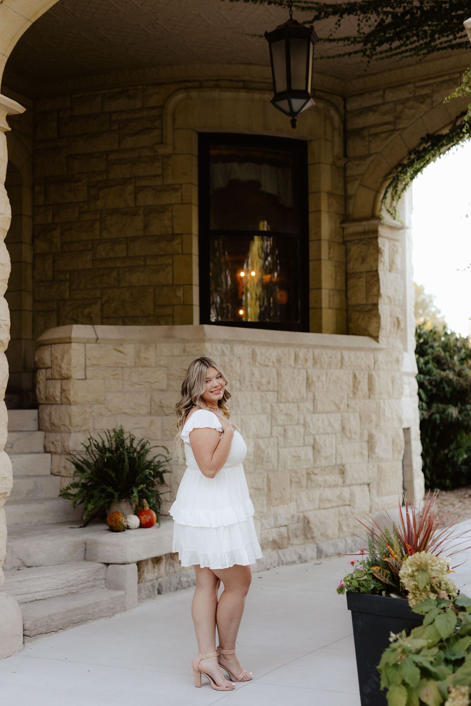 A white tiered dress is showcased against a stone entryway with lantern lighting and decorative planters.