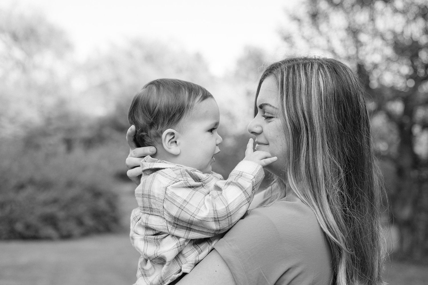 A tender black and white portrait of a parent and baby sharing an intimate moment outdoors.