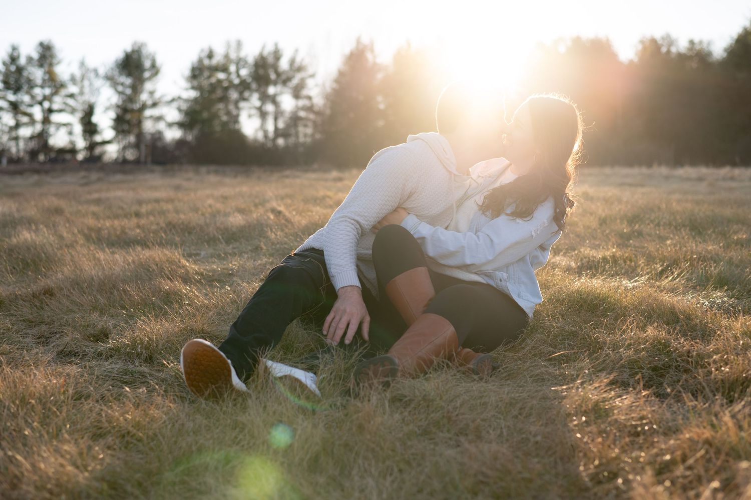 A couple relaxing together in a grassy field at sunset with sun flare.