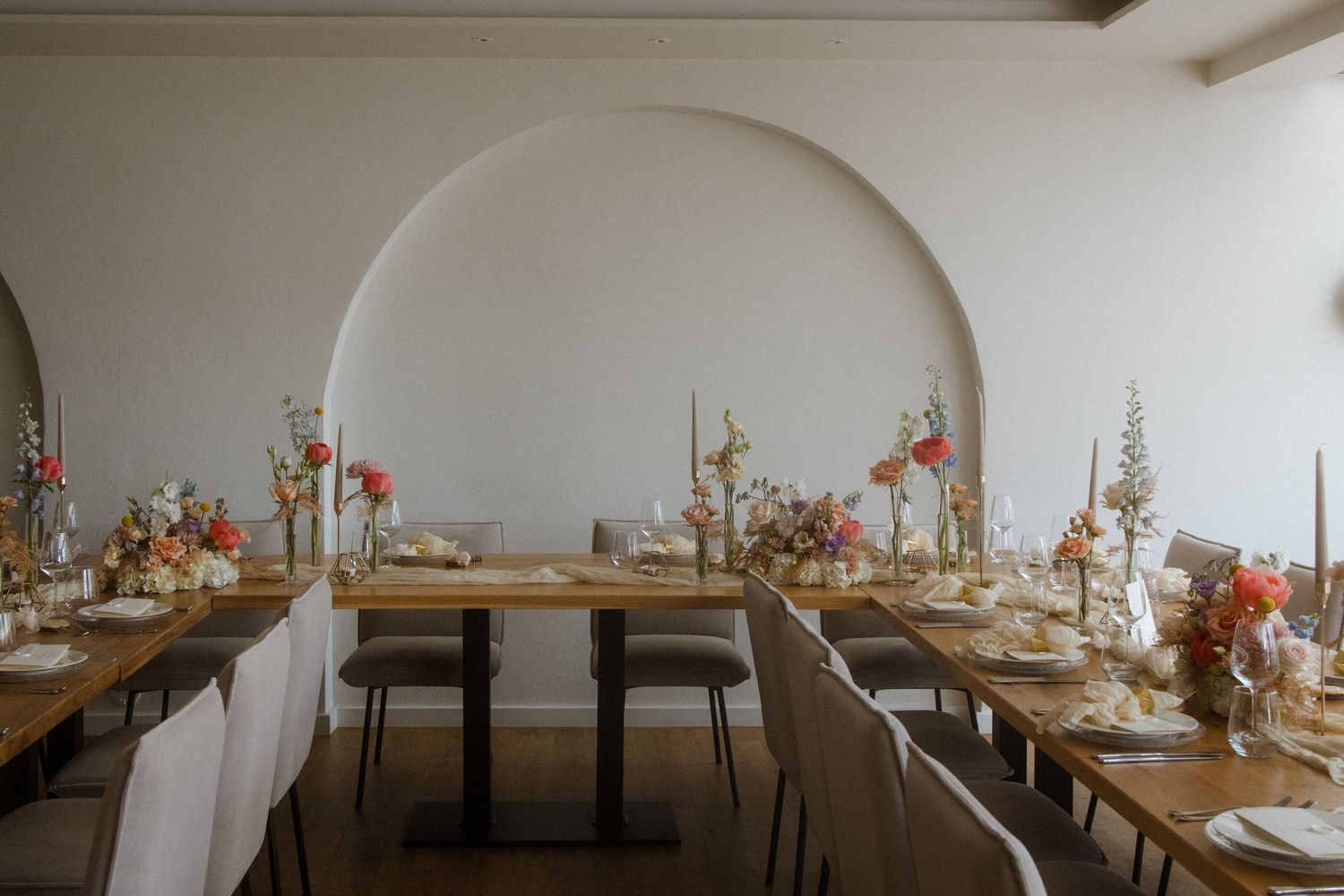 Modern minimalist restaurant interior with wooden tables and decorative floral arrangements on white walls.