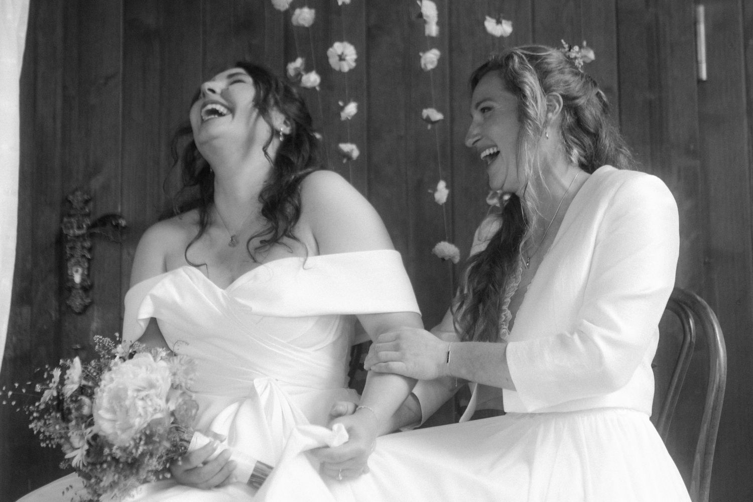 Black and white photo showing two joyful people sharing a candid laughing moment at a wedding ceremony.