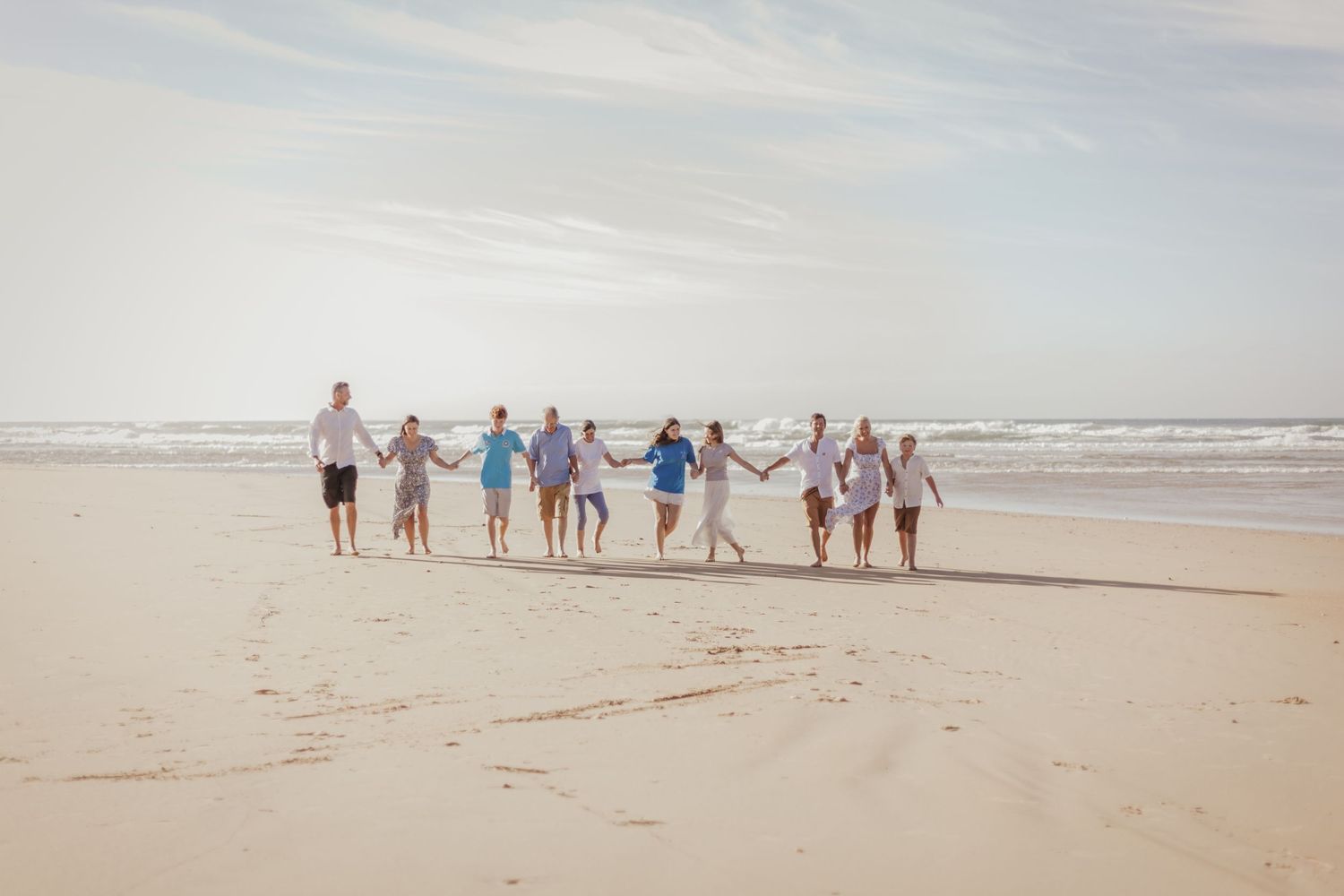 People holding hands while walking along a beach during sunset.
