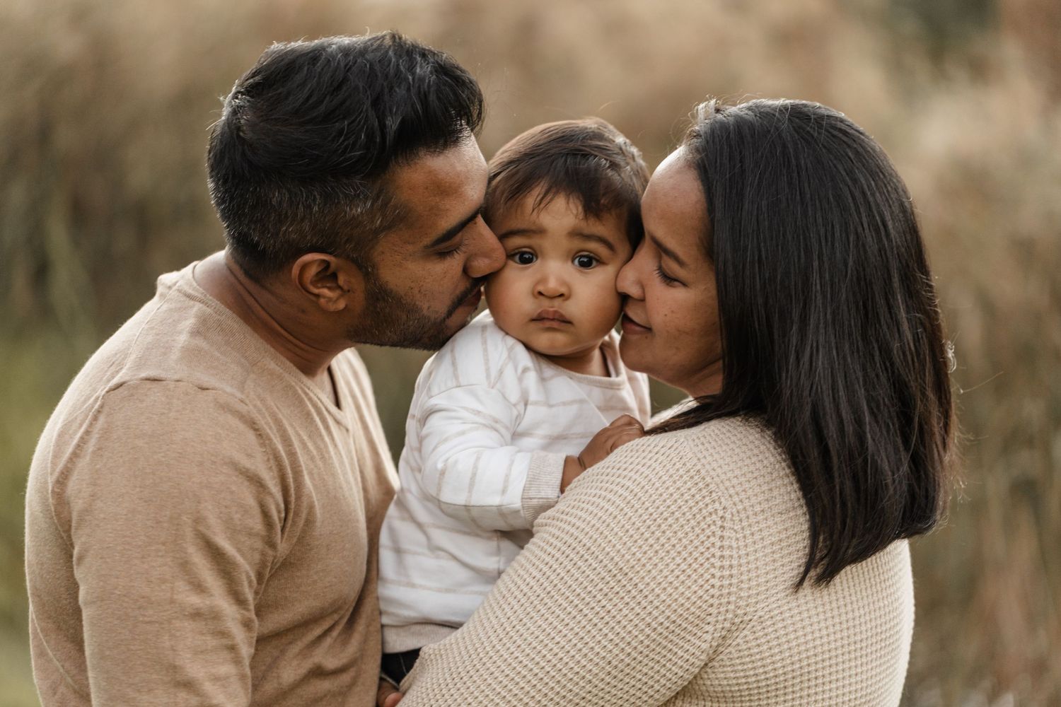 A family shares a tender moment together outdoors while wearing cozy beige and white sweaters.