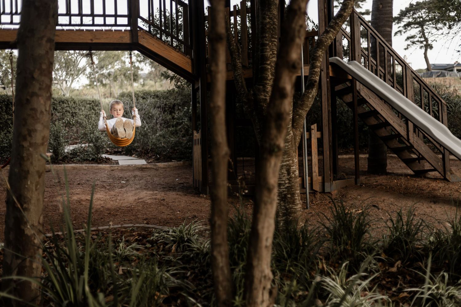 A tranquil swing chair hangs beneath a wooden staircase in a wooded outdoor setting during golden hour.