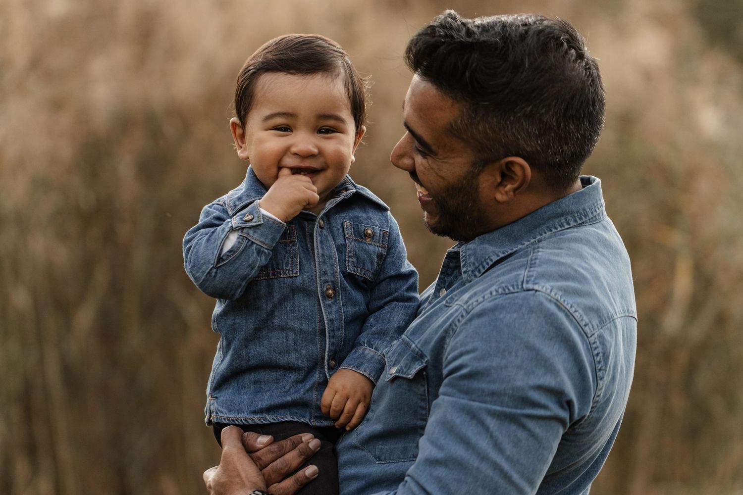 A joyful parent and toddler wearing matching denim jackets share a tender moment outdoors in autumn.