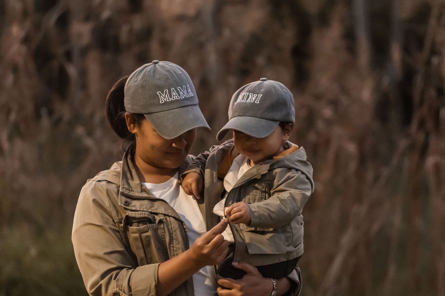 A parent and child wearing matching baseball caps share a tender moment outdoors in warm evening light.