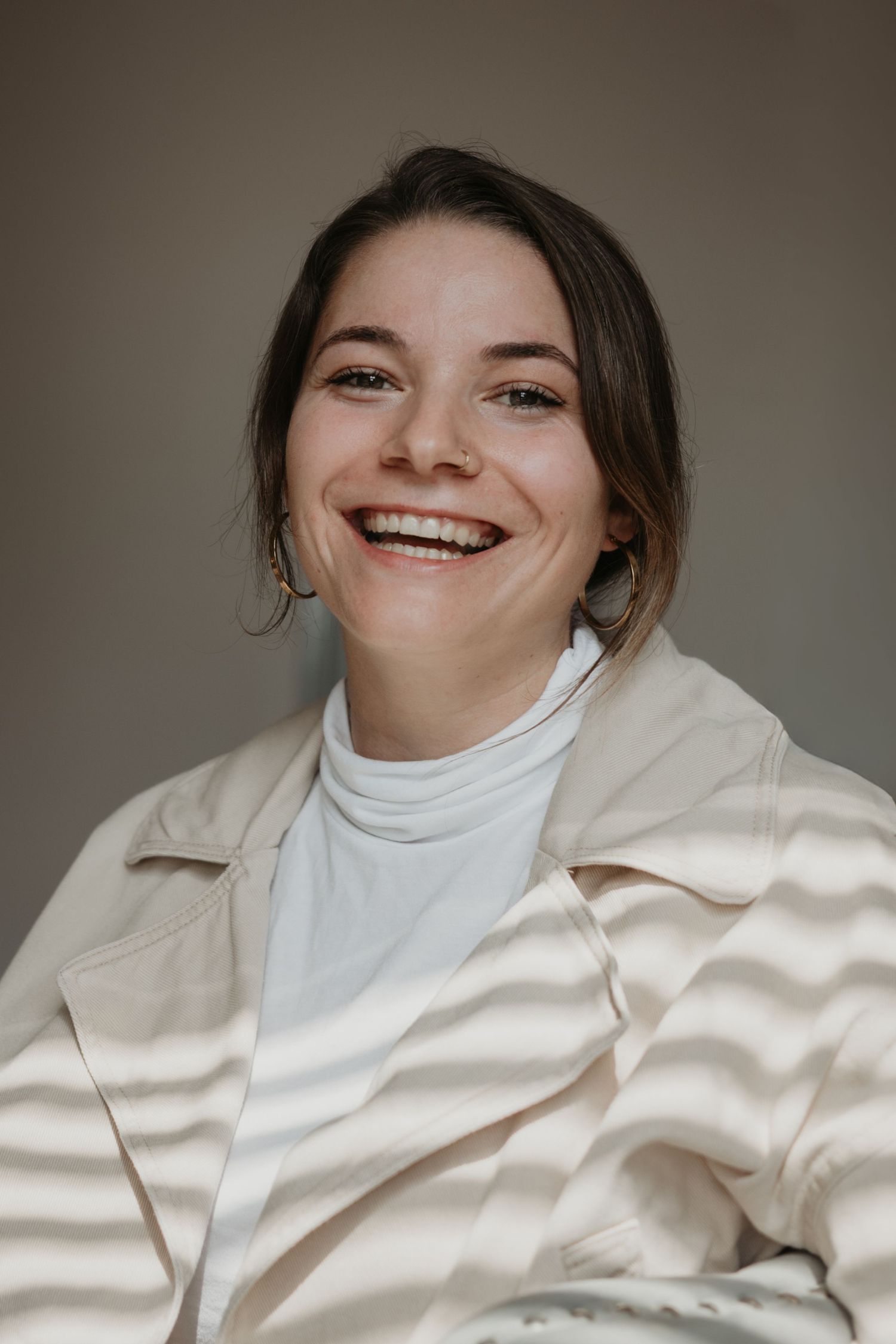 A series of candid expressions showing joy and laughter while wearing a white turtleneck and beige jacket.
