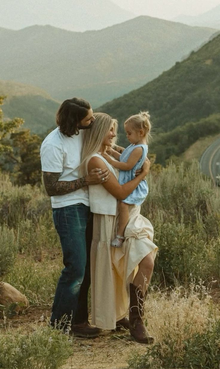 A family embraces together in a scenic mountain landscape with tall grass and golden sunlight.