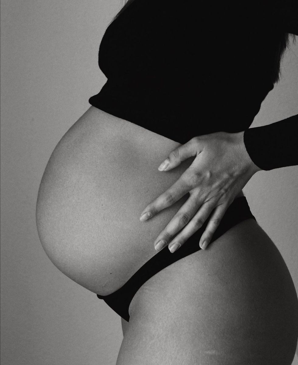 Black and white artistic photograph showing a pregnant belly with hands gently resting on the curved abdomen.
