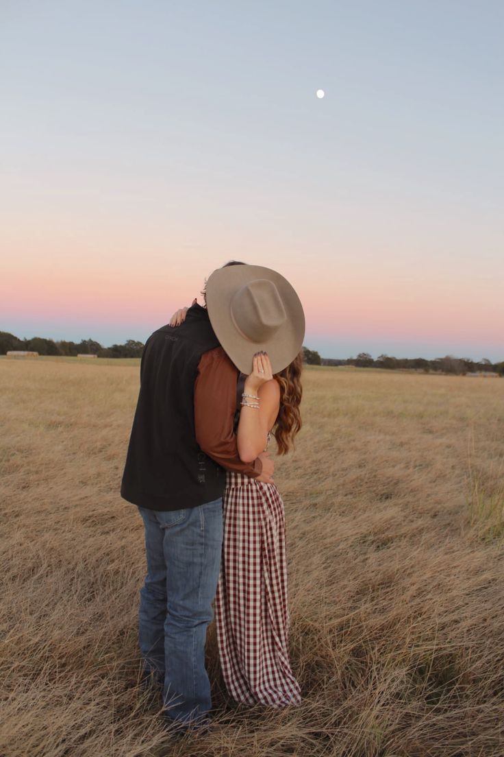 Two people share a romantic moment in a golden field at sunset while wearing casual western attire.
