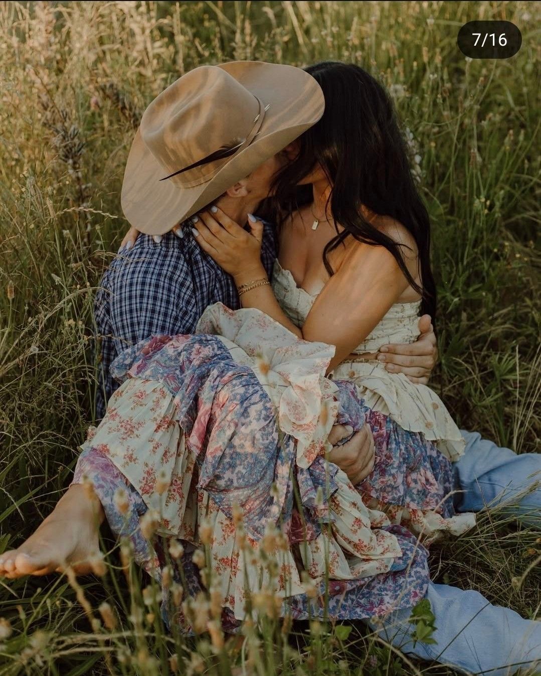 Couple sharing a romantic kiss in a wildflower meadow, woman in floral dress, man in cowboy hat and plaid shirt.