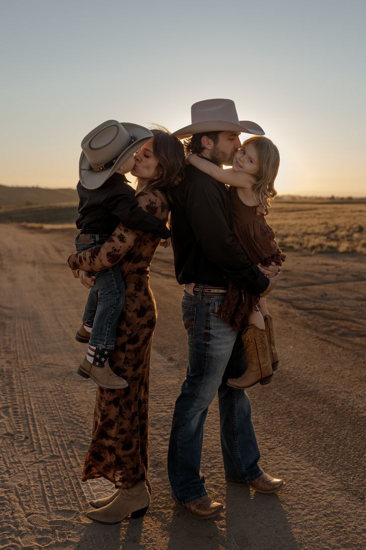 A family in western attire shares an intimate moment together on a dirt road at sunset.
