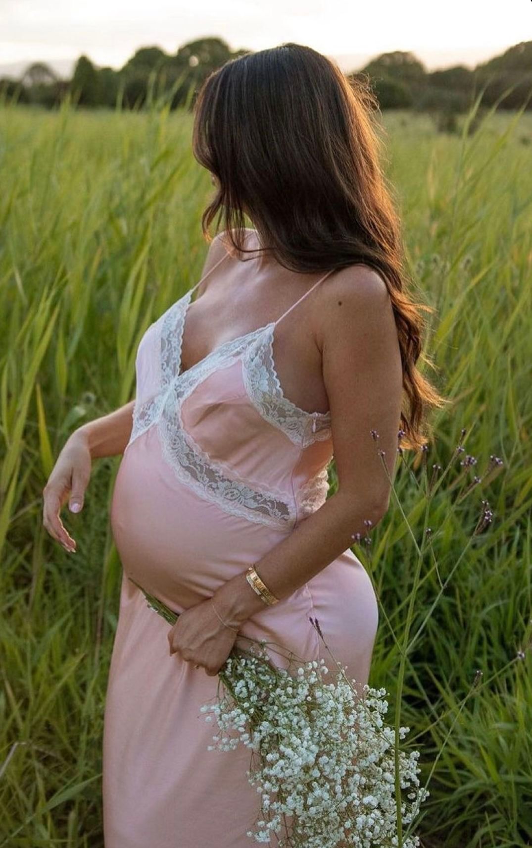 A person in a pink dress holds delicate baby's breath flowers while standing in a sunlit meadow of tall grass.