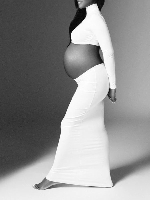 Black and white photo of a pregnant woman in white crop top and maxi skirt, showcasing her baby bump.
