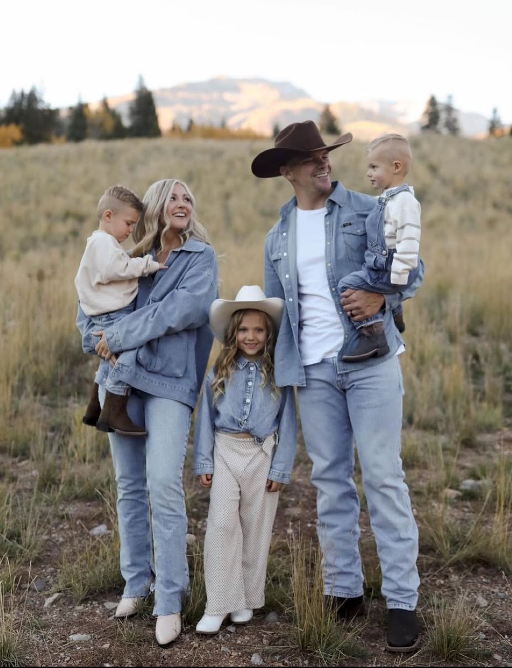 A group in denim outfits walks together on a grassy hillside during golden hour.